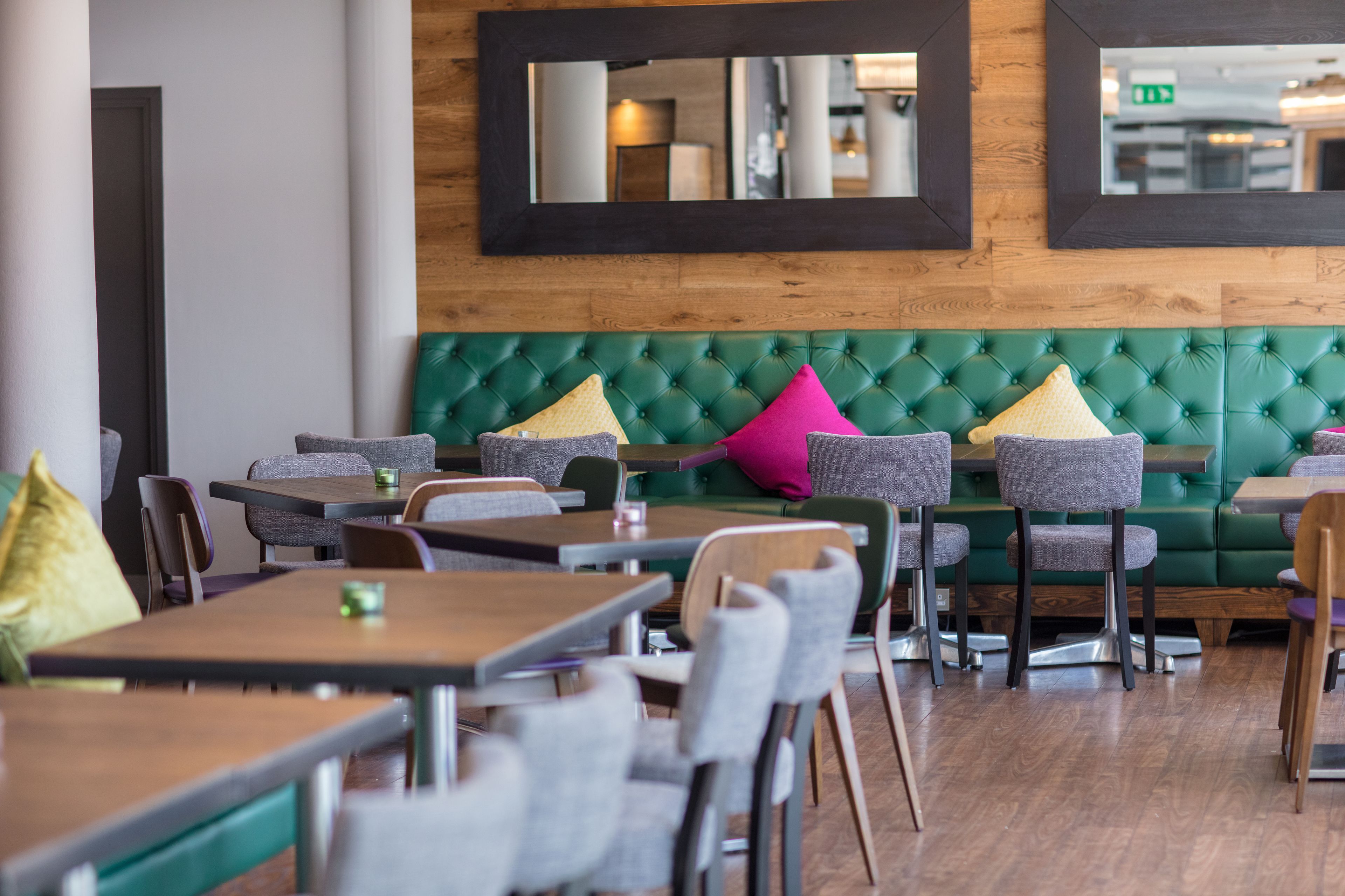 A restaurant with green upholstered booths, grey chairs, and wooden tables.