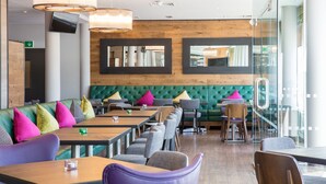 Um restaurante moderno com assentos estofados verdes, mesas de madeira e almofadas coloridas.