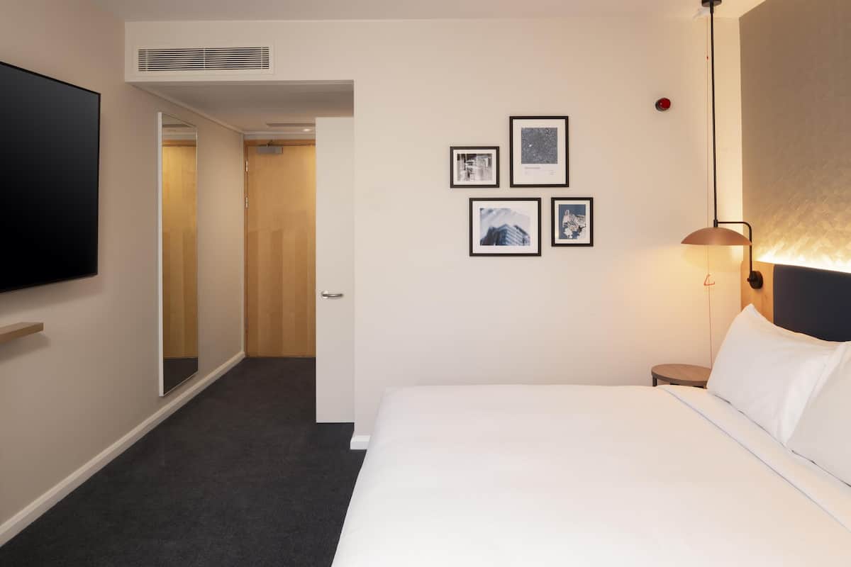 Een hotelkamer met een bed, een flatscreen televisie, een luchtventilator aan de muur en ingekaderde foto's.
