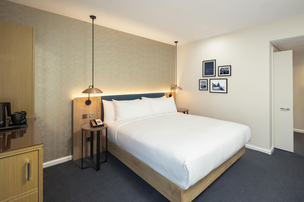 Een hotelkamer met een bed, nachtlampjes, een telefoon, een klein tafeltje en een kledingkast.