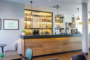 Een bar met een houten toonbank, planken met flessen en een koffieapparaat.