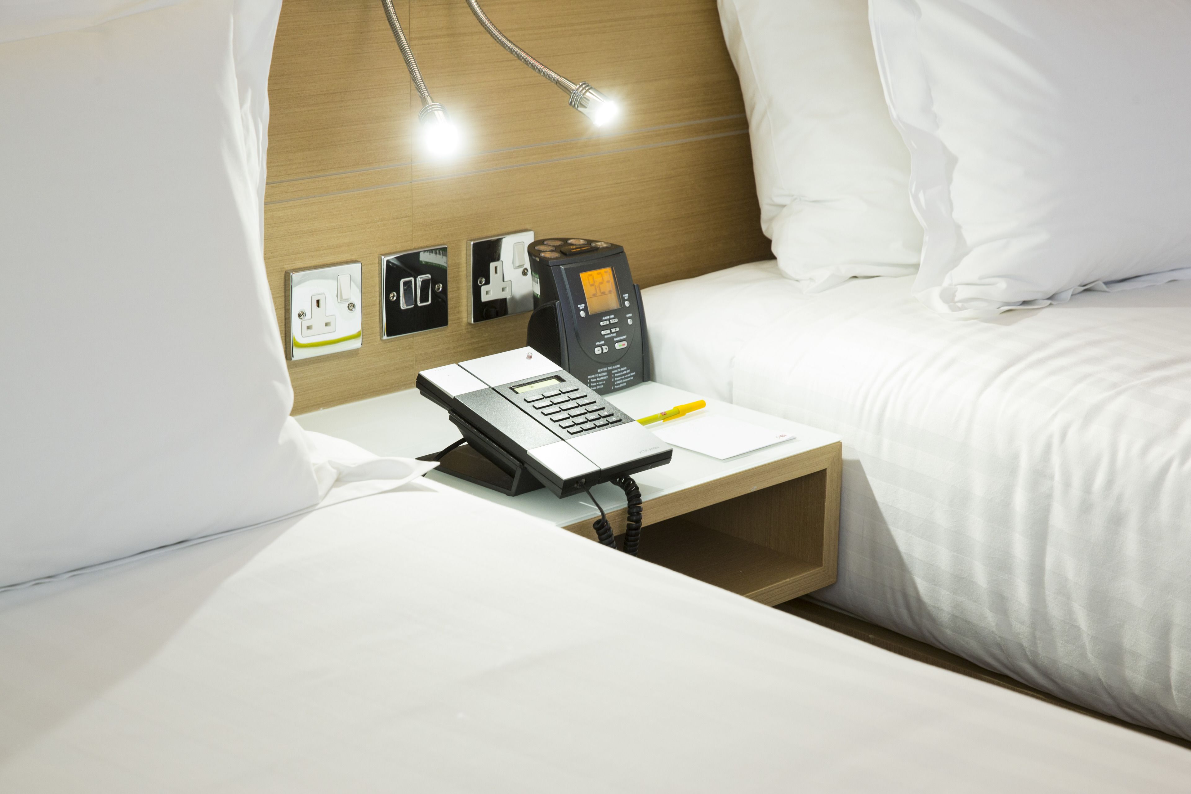 Een hotelkamer met een bureau, telefoon, koffiezetapparaat en een stopcontact.