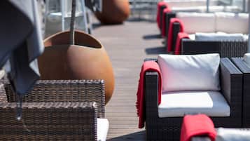 A row of wicker lounge chairs with red and white cushions on a wooden deck.