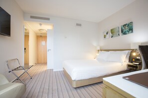 Ein Hotelzimmer mit Bett, Schreibtisch, Sessel, Fernseher und Bildern an der Wand.