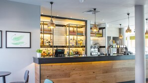 Uma área de bar com balcão de madeira, prateleiras com garrafas e luminárias pendentes.