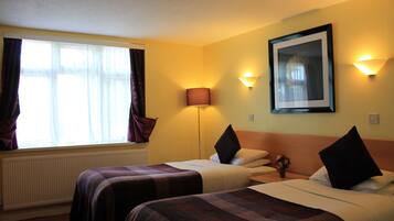 Une chambre d’hôtel avec deux lits, une grande fenêtre avec des rideaux, une lampe sur pied et un tableau encadré au mur.