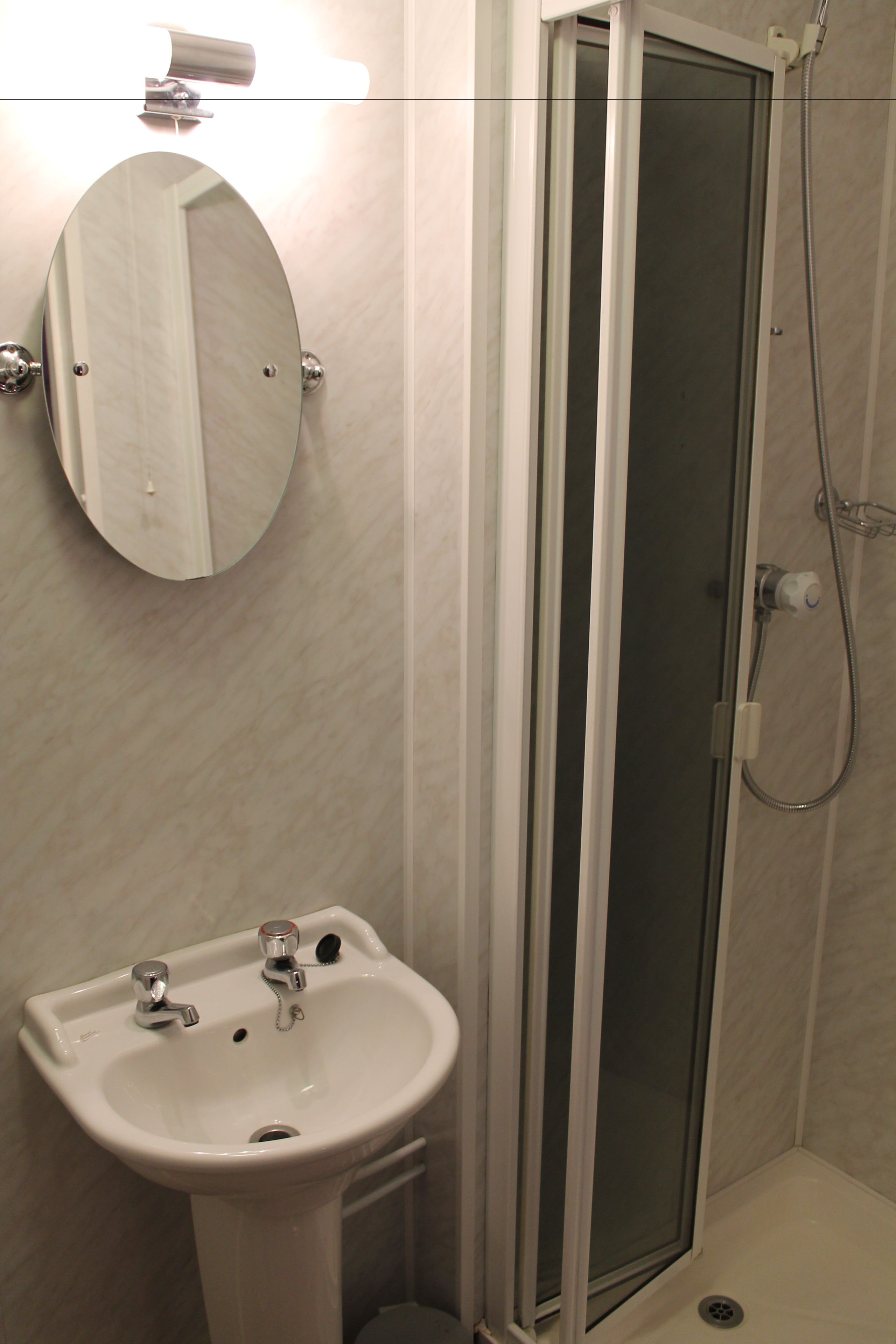 Un baño con lavamanos blanco, espejo y ducha con mampara de vidrio.
