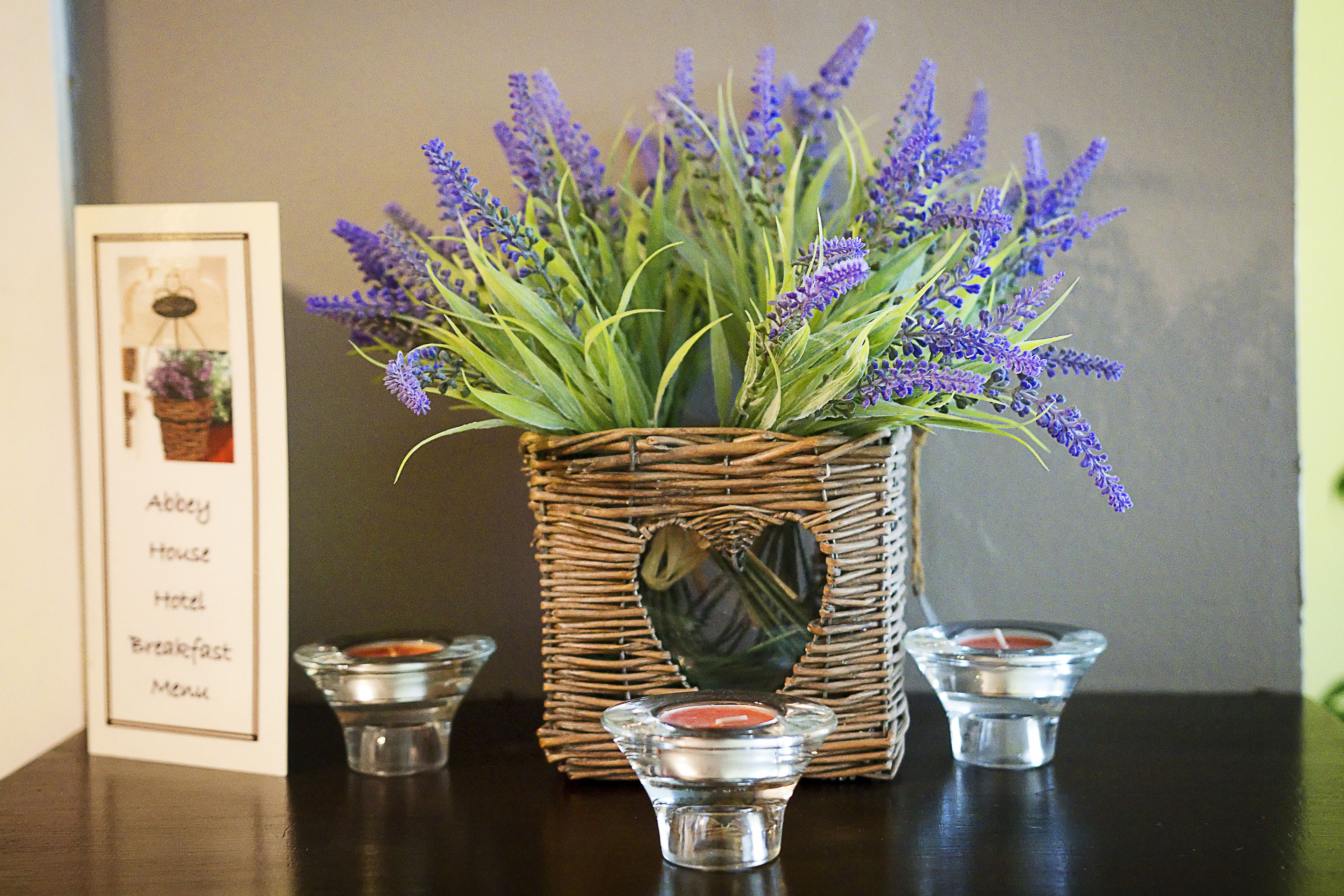 A wicker basket with lavender flowers, two candle holders, and a framed menu on a table.