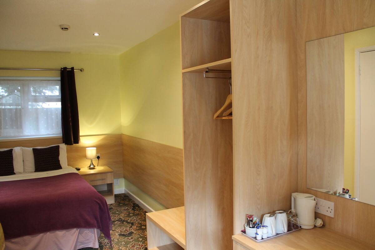A hotel room with a bed, bedside table, lamp, and a wooden wardrobe.