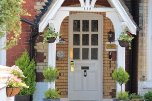 A white door with a grid pattern, flanked by brick walls and a white archway. There are hanging flower baskets on either side of the door. - Abbey House Hotel (Reading)