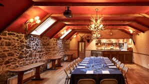 A dining area with a long table set for a meal, wooden beams on the ceiling, stone walls, and a bar area in the background. - Loch Kinord Hotel (Aboyne)