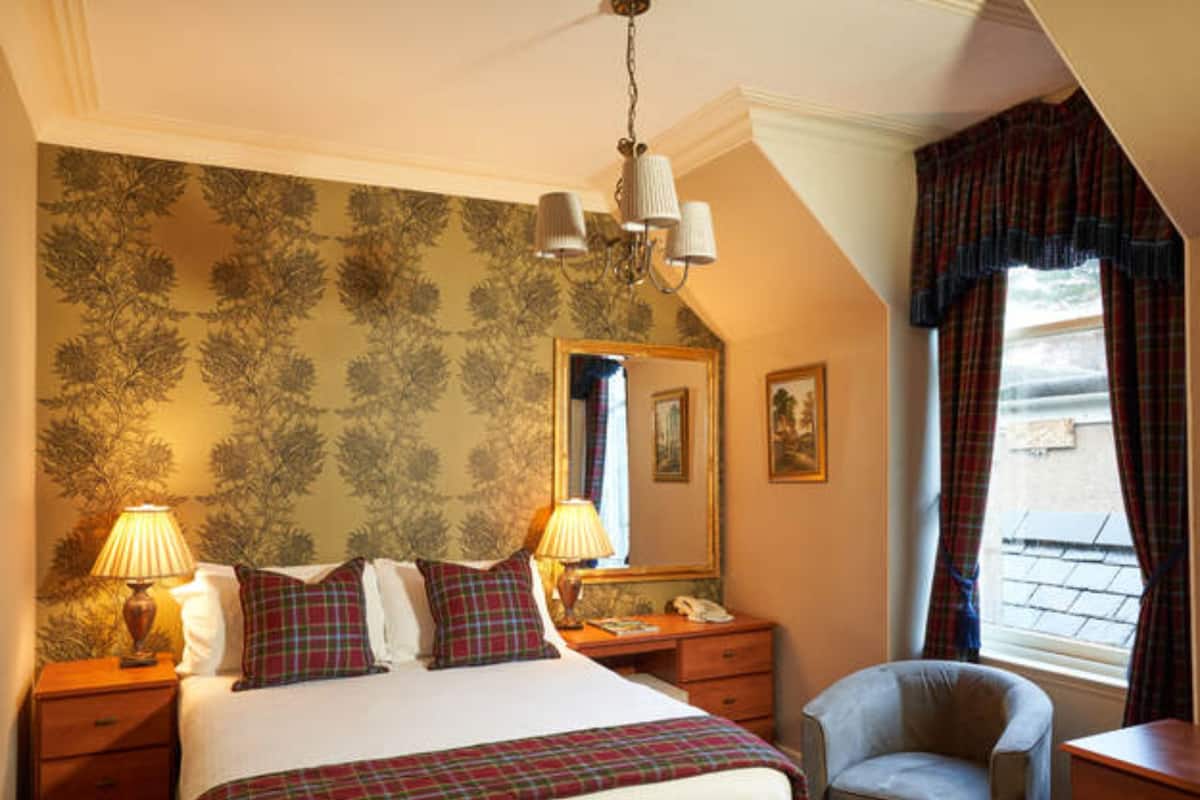 A bedroom with a bed, two bedside tables, a chair, a desk, a mirror, and a window with curtains.