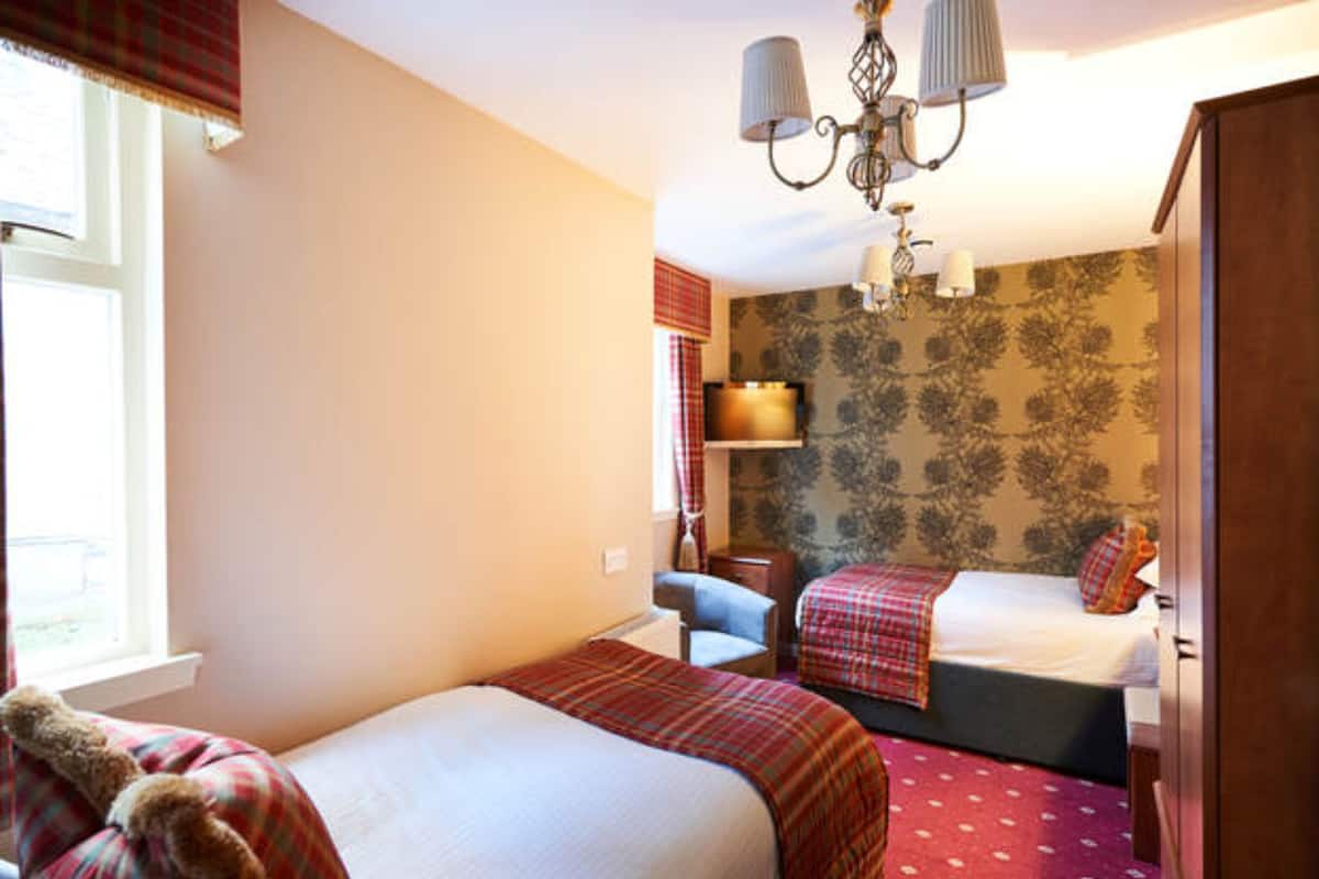 A bedroom with two beds, a window with curtains, a chandelier, and a television on a stand.