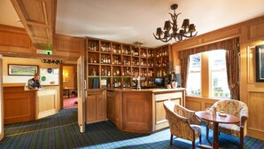 A bar area with wooden shelves stocked with bottles, a bar counter, and a seating area with a plaid carpet. - Loch Kinord Hotel (Aboyne)