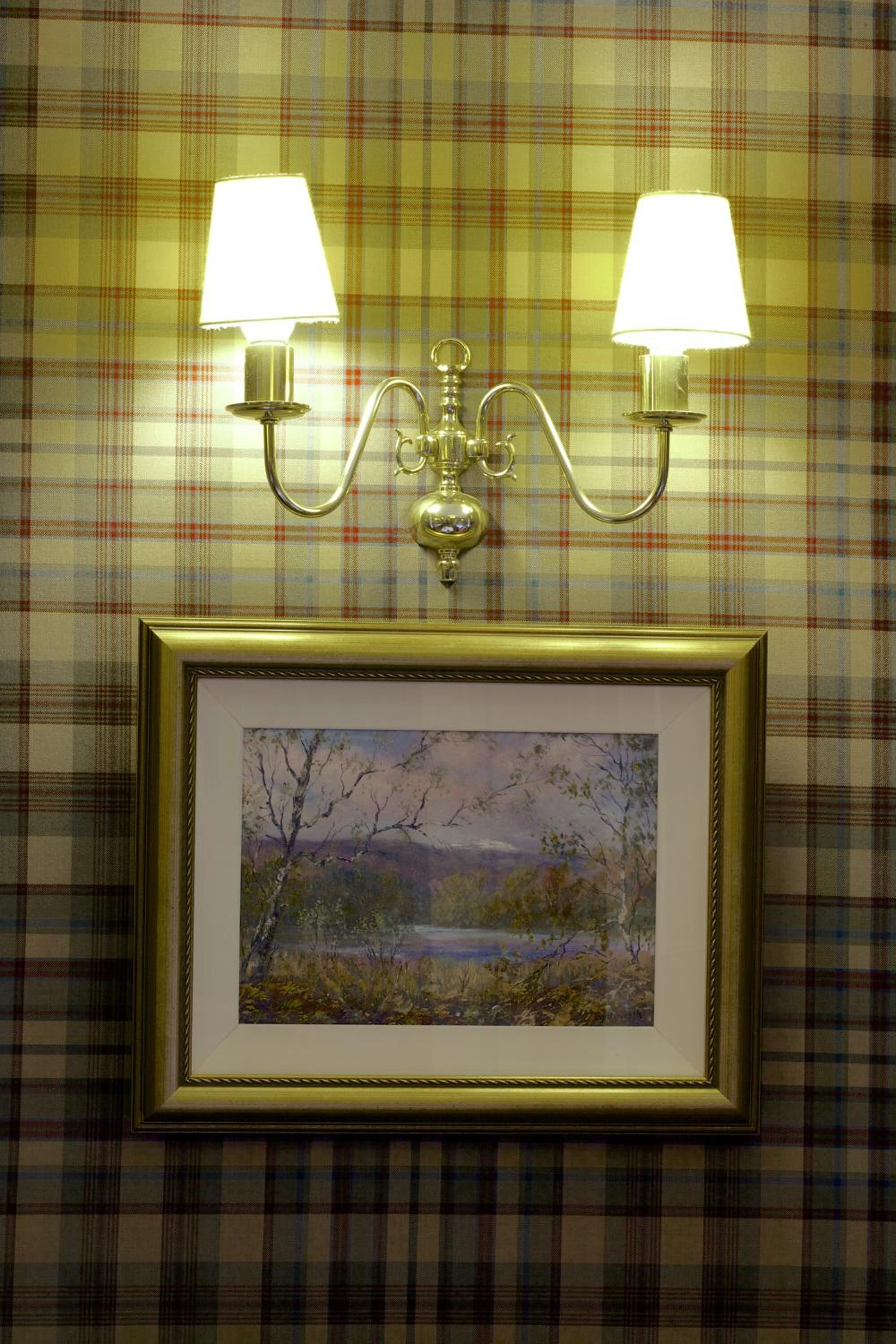 Una lámpara de pared con dos luces y un cuadro con un paisaje.