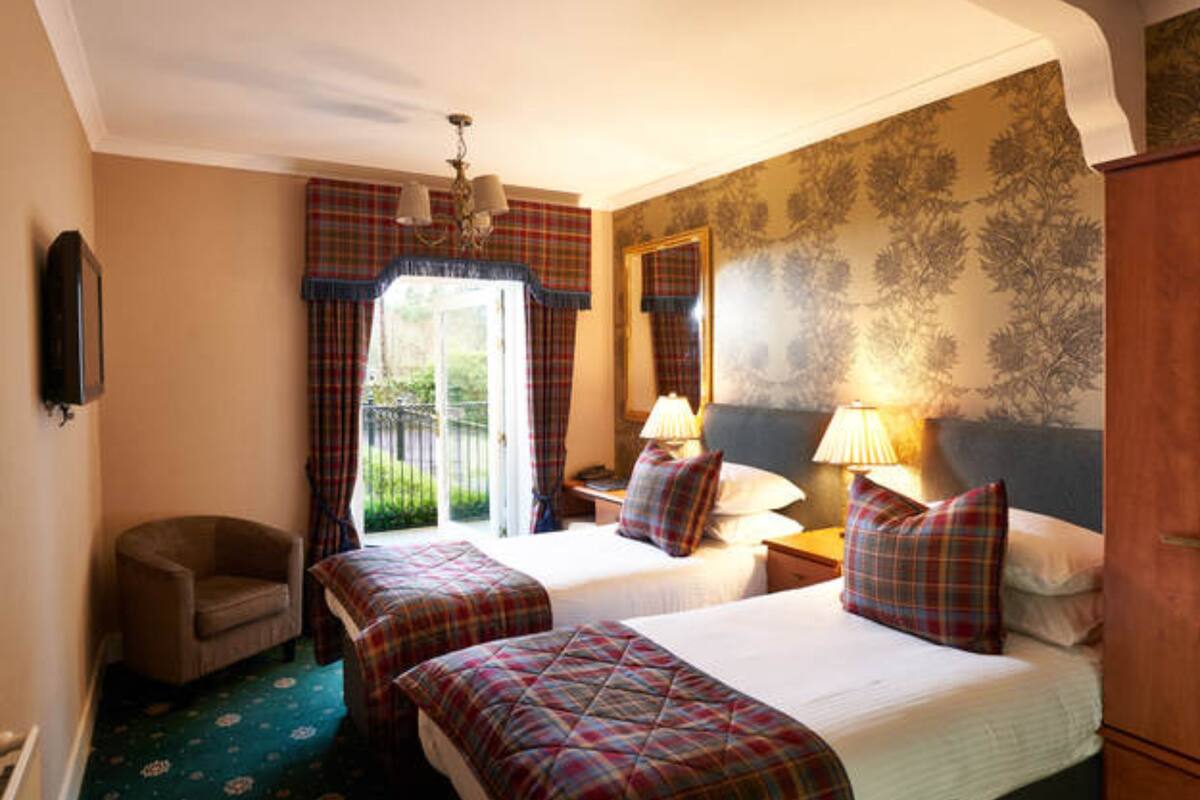 A hotel room with two beds, a chair, a desk, and a large window with curtains.