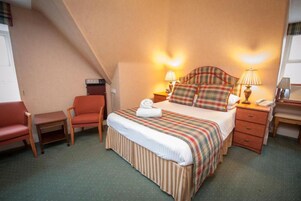 Una habitación de hotel con una cama, dos mesitas de noche, una silla y una pequeña mesa.