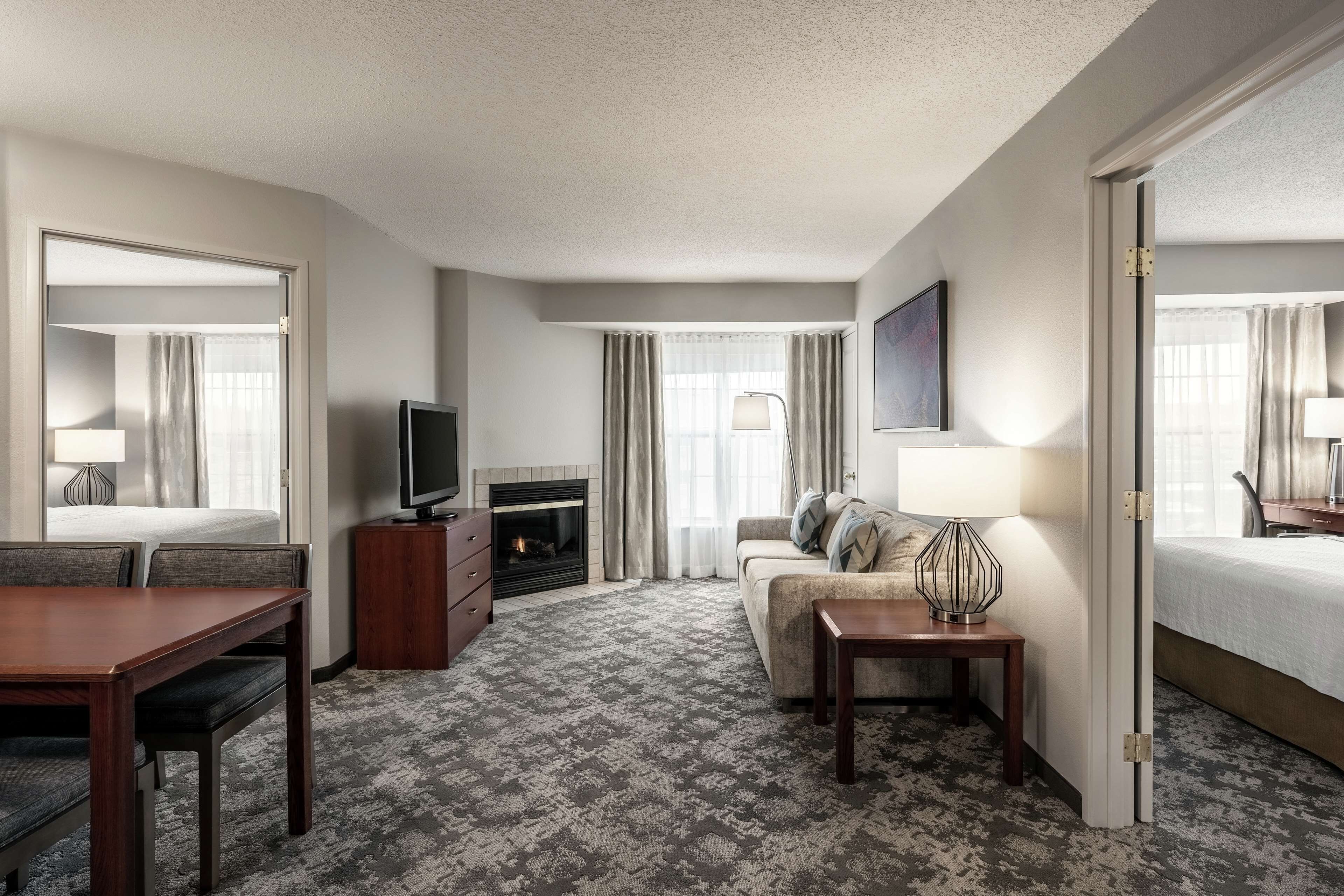 A hotel room with a bed, a sofa, a TV, a fireplace, and a dining area.