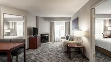 A hotel room with a bed, a sofa, a TV, a fireplace, and a dining area.