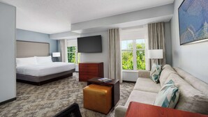 A hotel room with a bed, a sofa, a coffee table, a TV, and a window with curtains. - Homewood Suites by Hilton Erie (Erie)