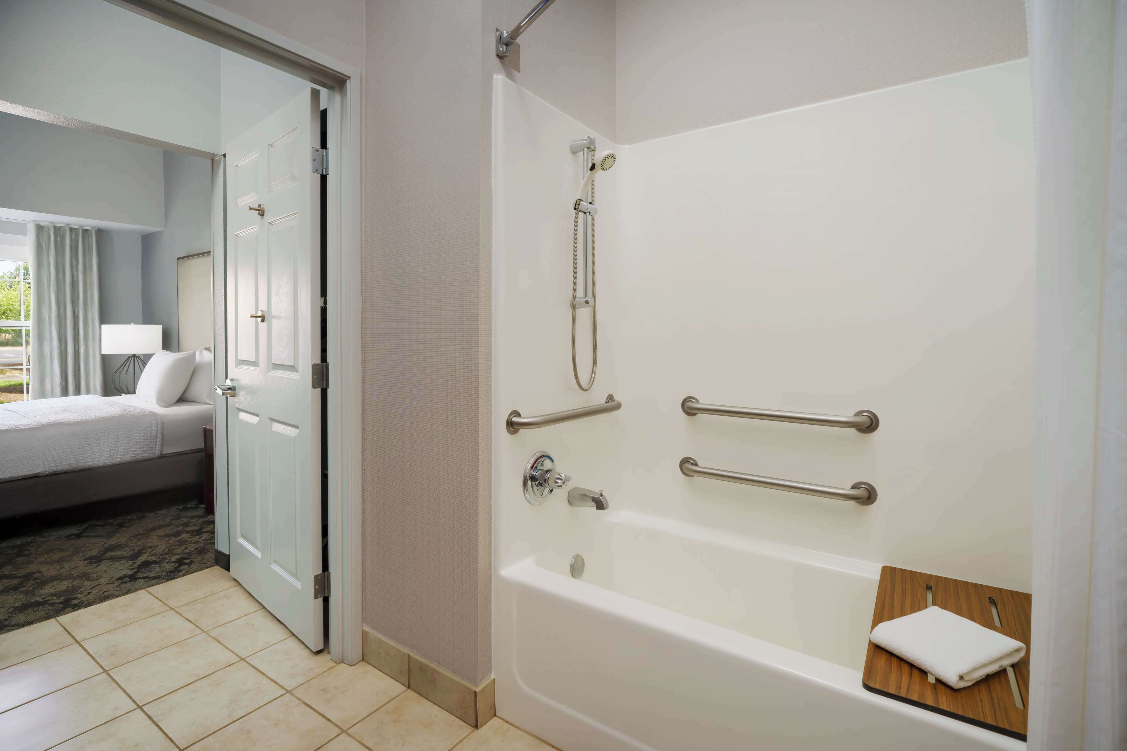 A hotel bathroom with a bathtub, handrails, and a towel rack.