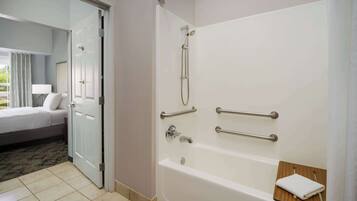 A hotel bathroom with a bathtub, handrails, and a towel rack.