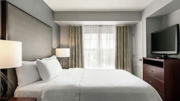 A hotel room with a large bed, two bedside lamps, a flat-screen TV, and a view of the city through sheer curtains.
