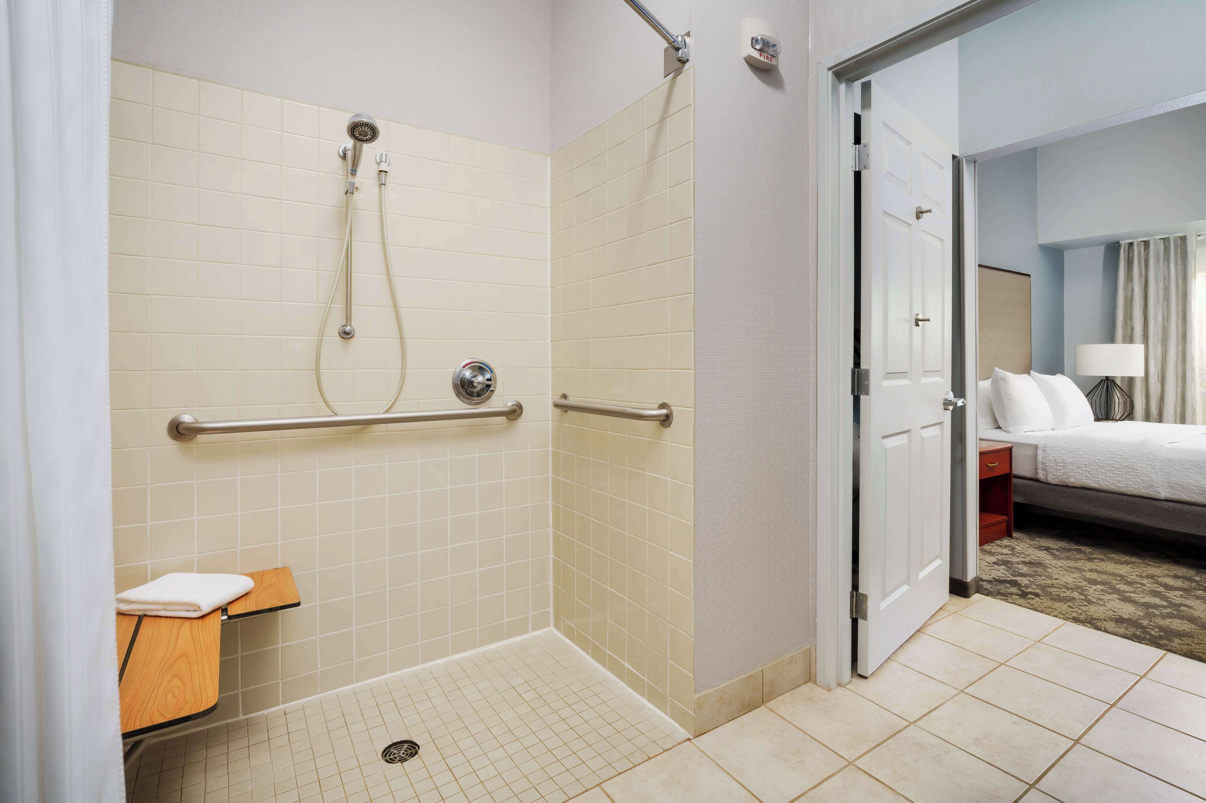 Un baño de hotel con ducha, barras de apoyo, inodoro y lavamanos.