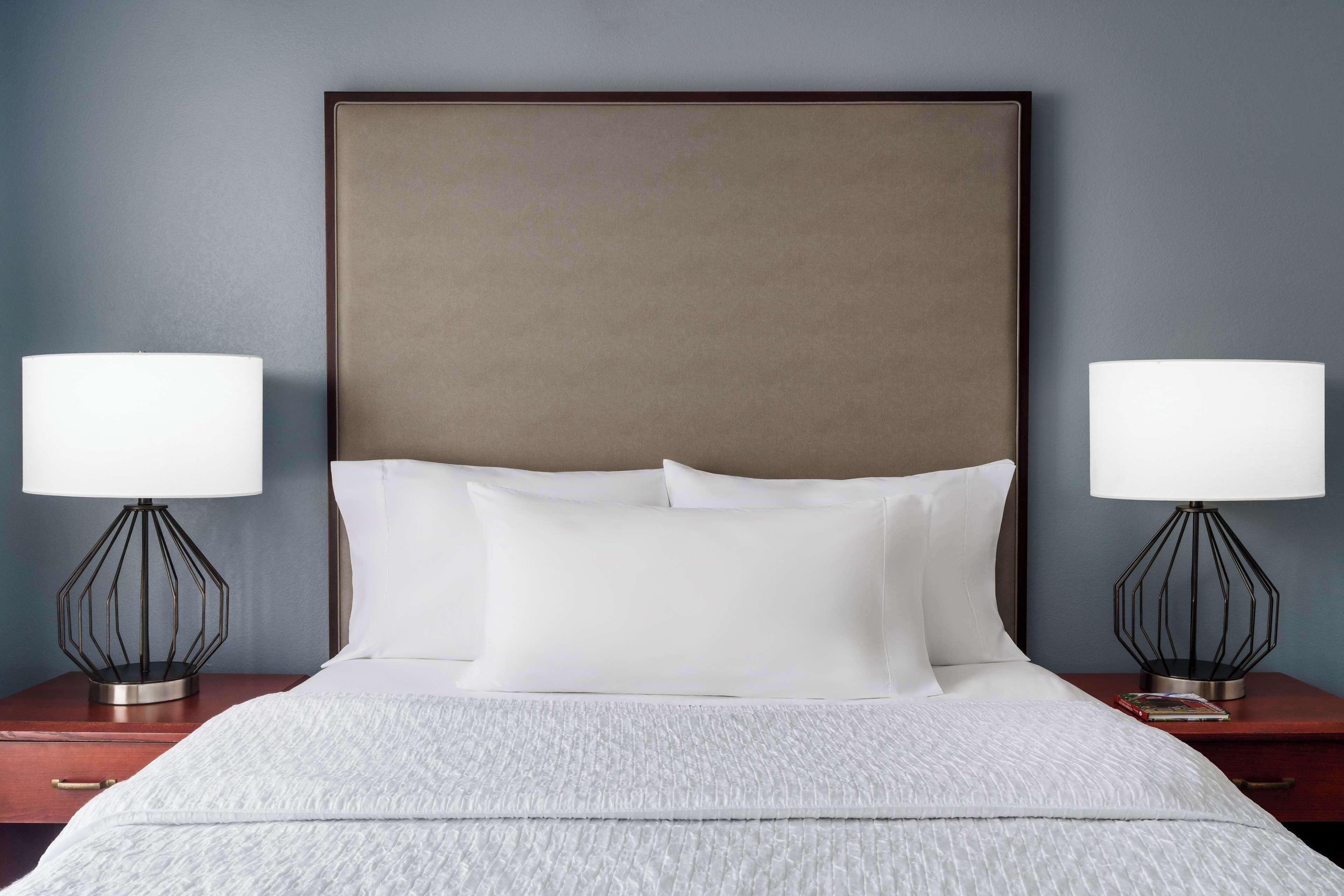 A neatly made bed with white linens, two bedside tables with lamps, and a large headboard.
