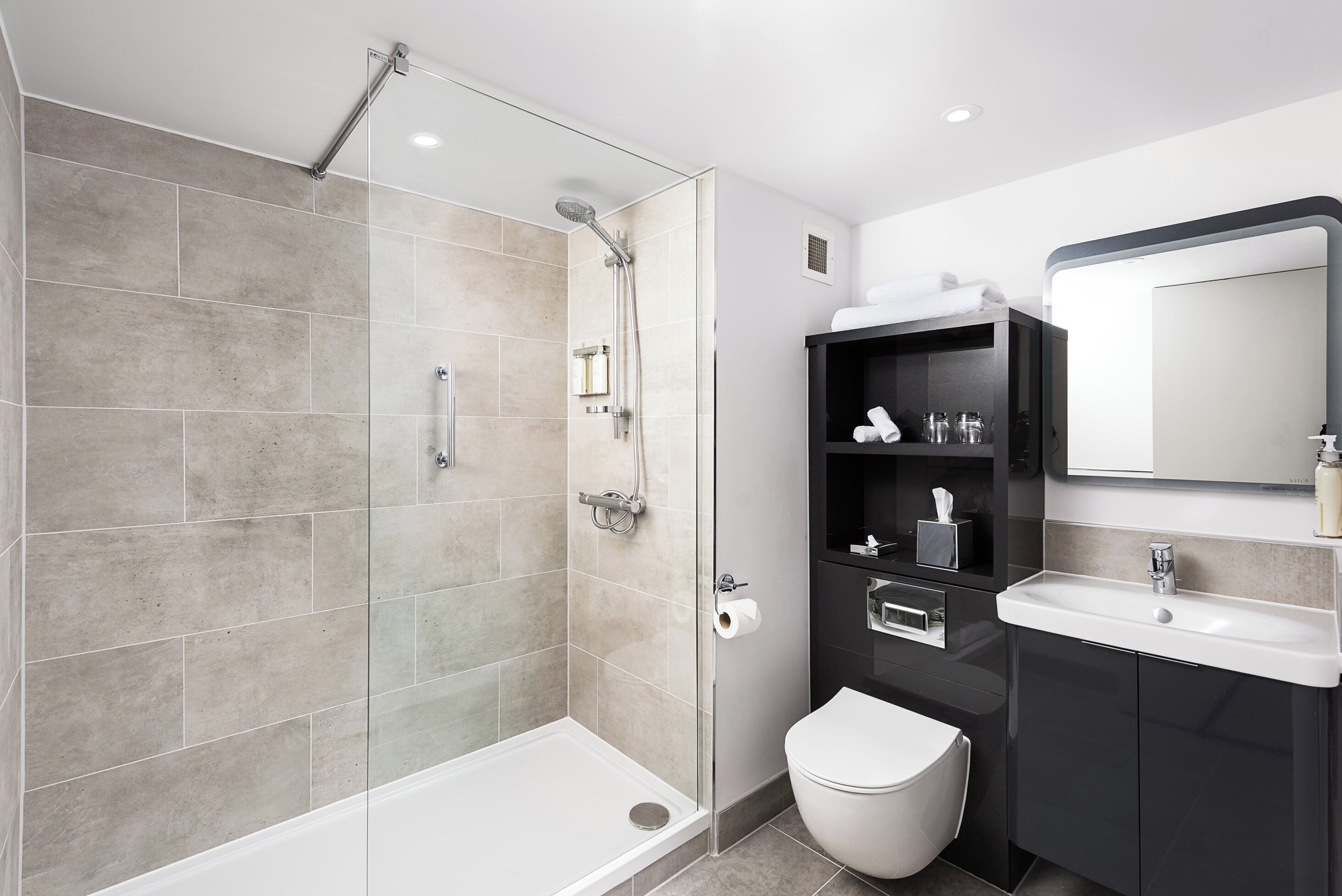 Une salle de bain moderne avec une douche à parois de verre, des toilettes et un meuble-lavabo avec un miroir.