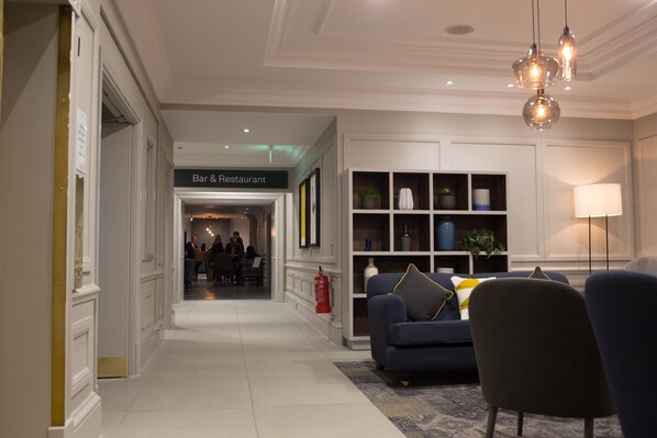 A hotel lobby with a Bar & Restaurant sign, a fire extinguisher, a sofa, and a lamp.