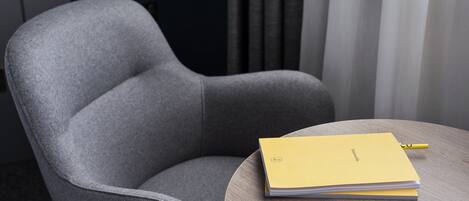 A grey upholstered armchair with a wooden table beside it, holding a yellow folder and a pen.