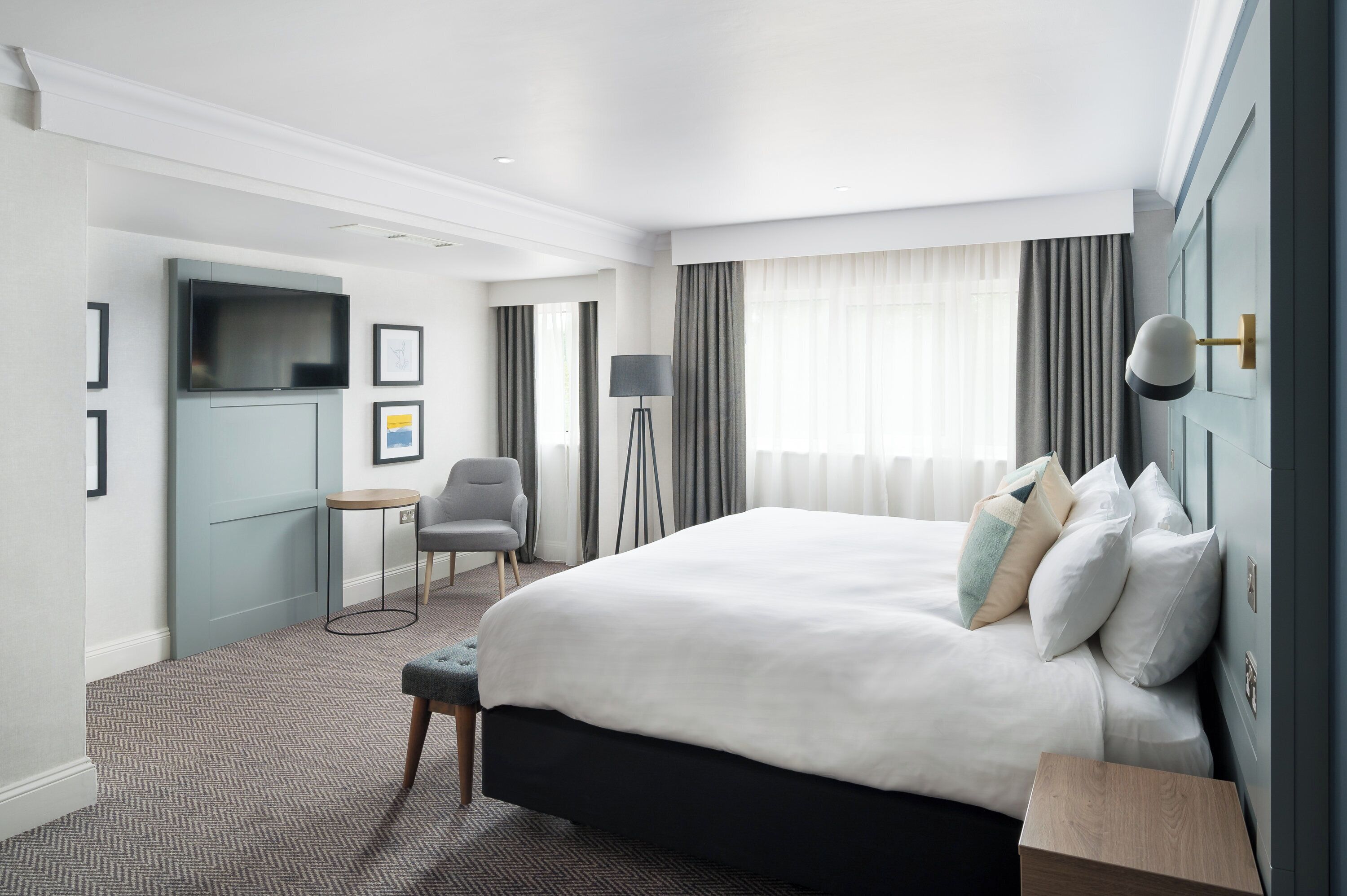 A hotel room with a large bed, a desk, a chair, a TV, and a window with curtains.