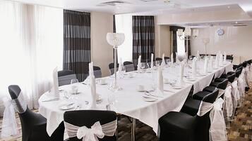 Una larga mesa banquete dispuesta con manteles blancos, sillas negras con cintas blancas y candelabros de cristal.