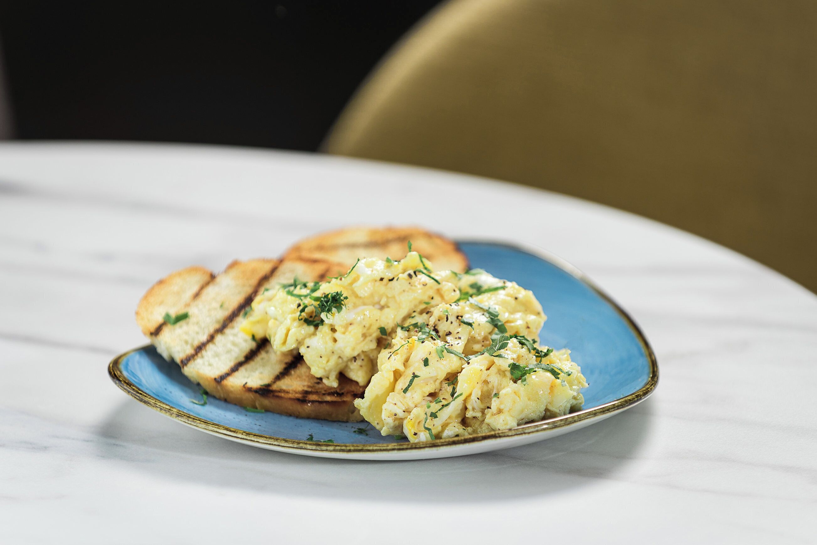 Un plato con huevos revueltos y tostadas sobre un plato con borde azul.