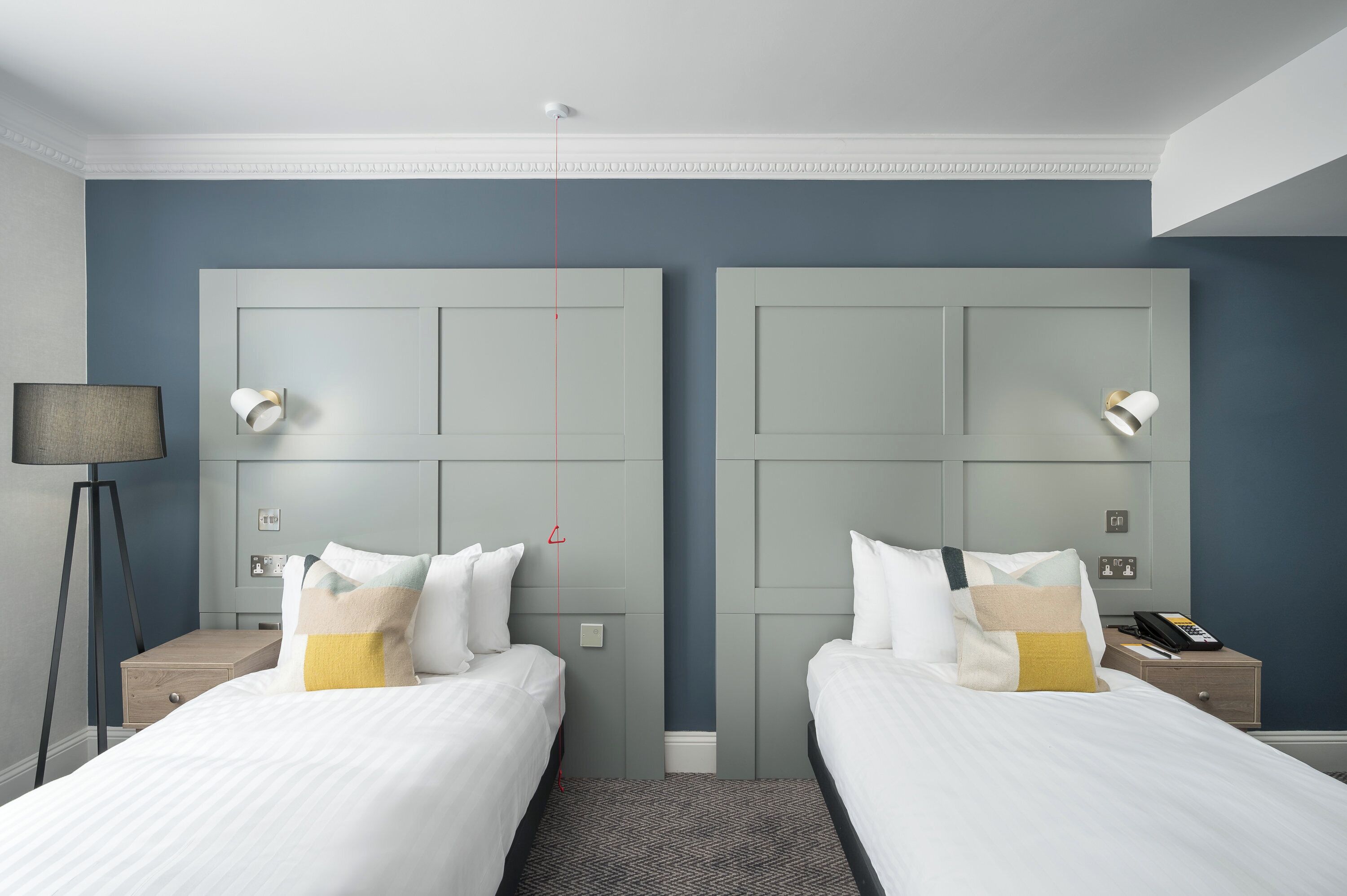 A hotel room with two beds, a nightstand with a lamp, a phone, and a small table.