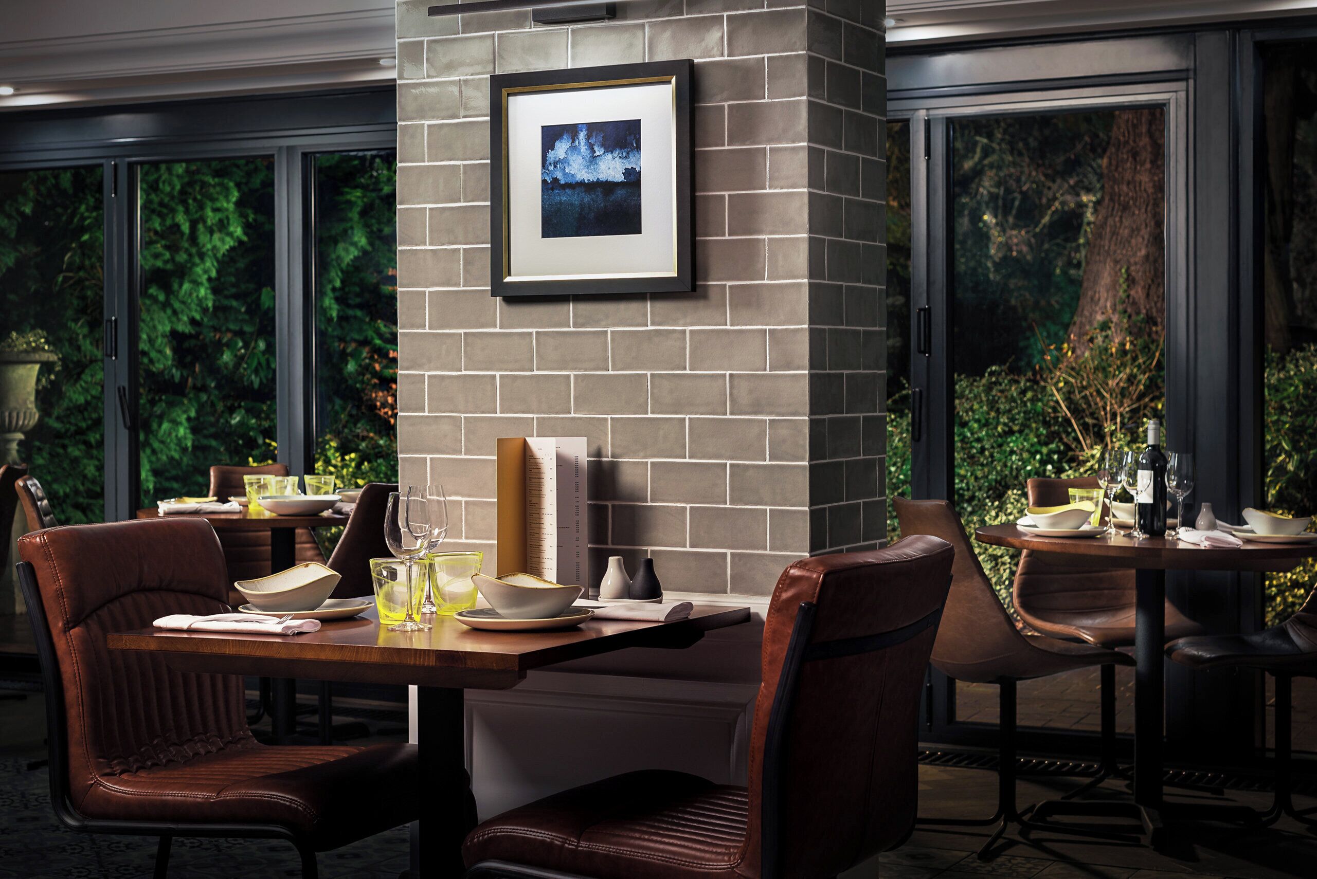 A dining area with brick walls, framed artwork, and a view of greenery through large windows.