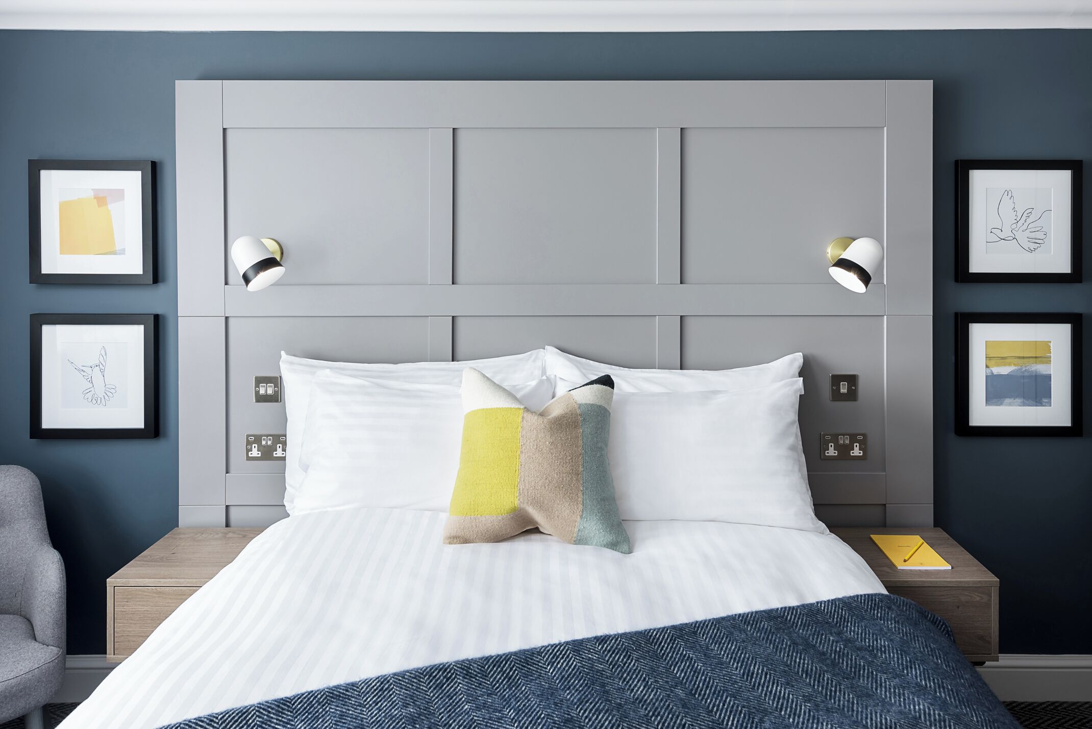A hotel room with a large bed, two bedside tables, a chair, and artwork on the walls.