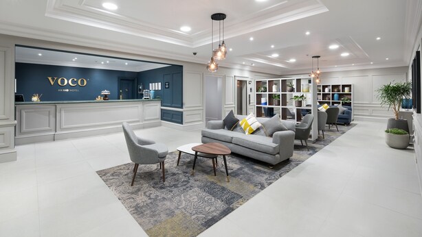 A modern hotel lobby with a reception desk, seating area, and a bookshelf.