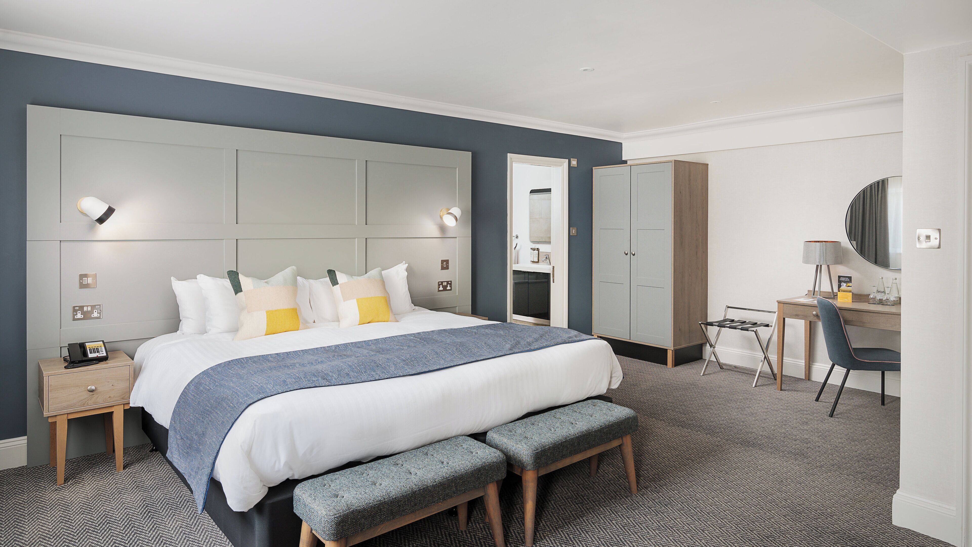 Een hotelkamer met een groot bed, nachtkastjes, een bureau, een stoel, een kledingkast en een spiegel.