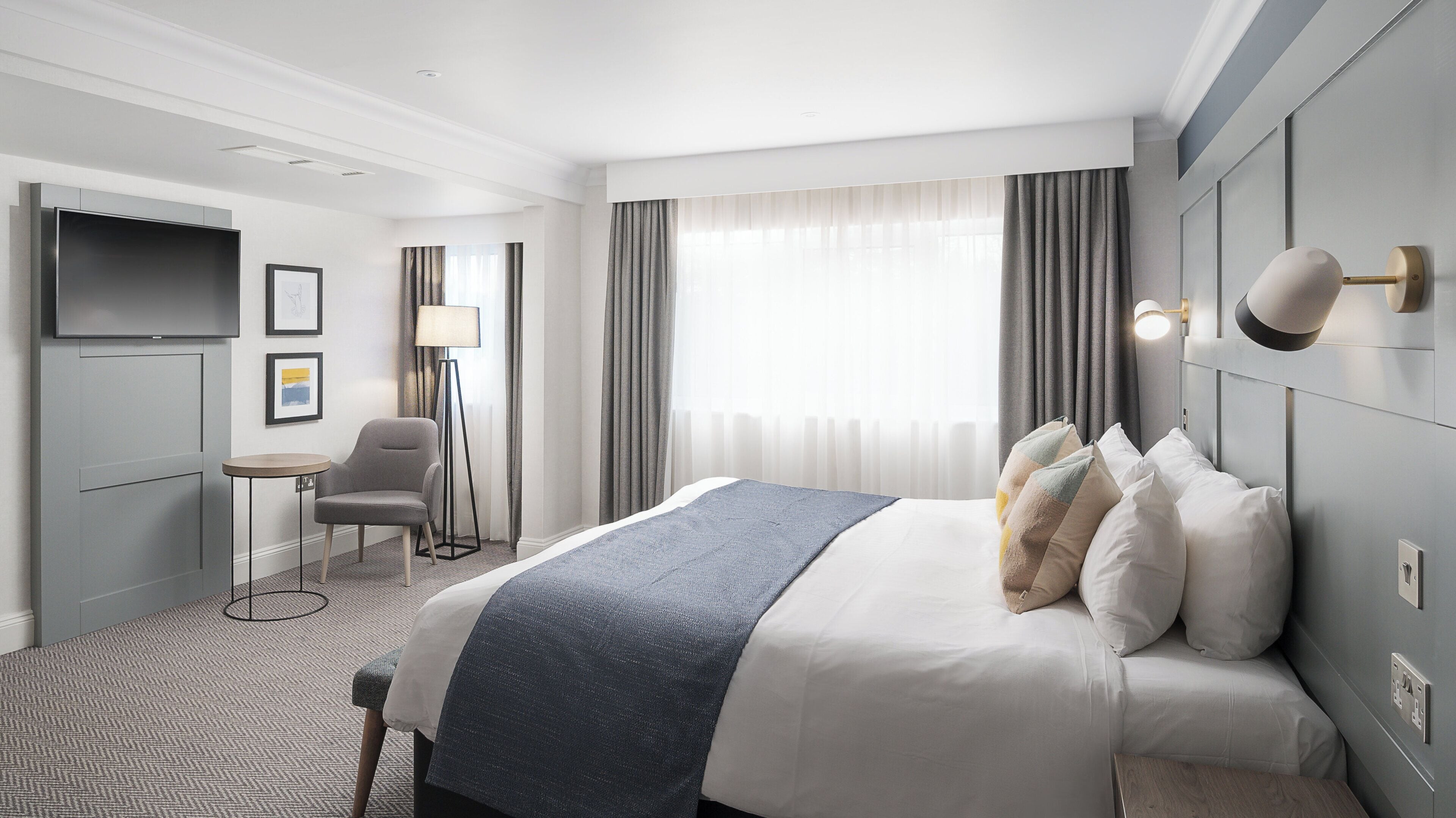 Ein Hotelzimmer mit Bett, Schreibtisch, Stuhl, Fernseher und einem Fenster mit Vorhängen.