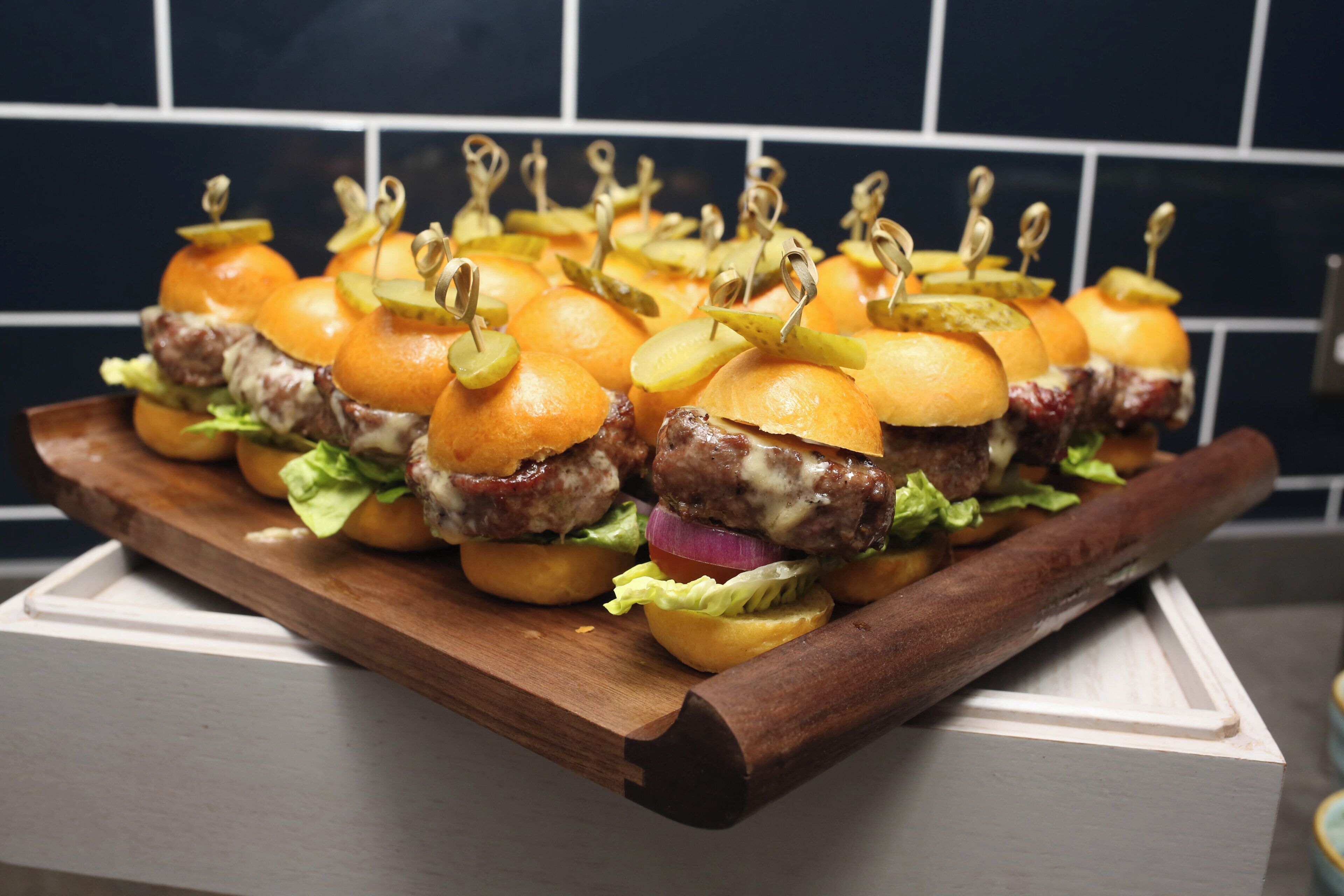 Una tabla de madera con una hilera de hamburguesas, cada una con pan, lechuga y una loncha de queso.