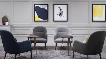 A room with three armchairs and two small tables, a potted plant, and three framed artworks on the wall.