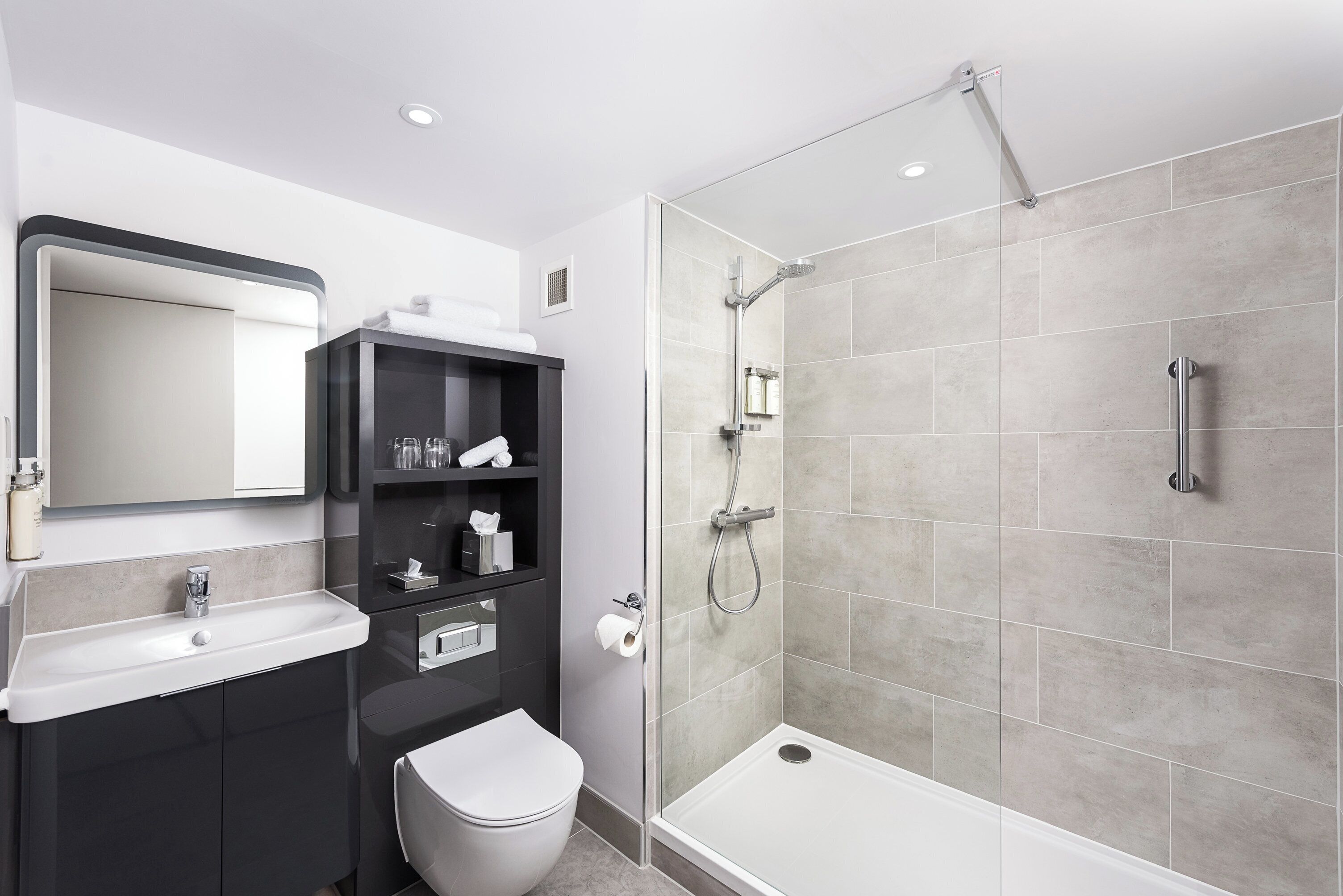 Ein modernes Badezimmer mit Dusche, Toilette, Waschbecken und einem Spiegel darüber.
