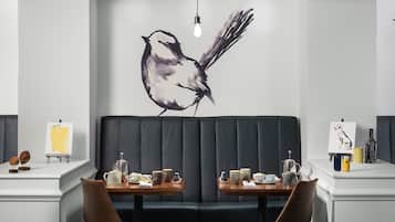 Un comedor moderno con un gran mural de un pájaro, dos mesas con sillas y una lámpara colgante.
