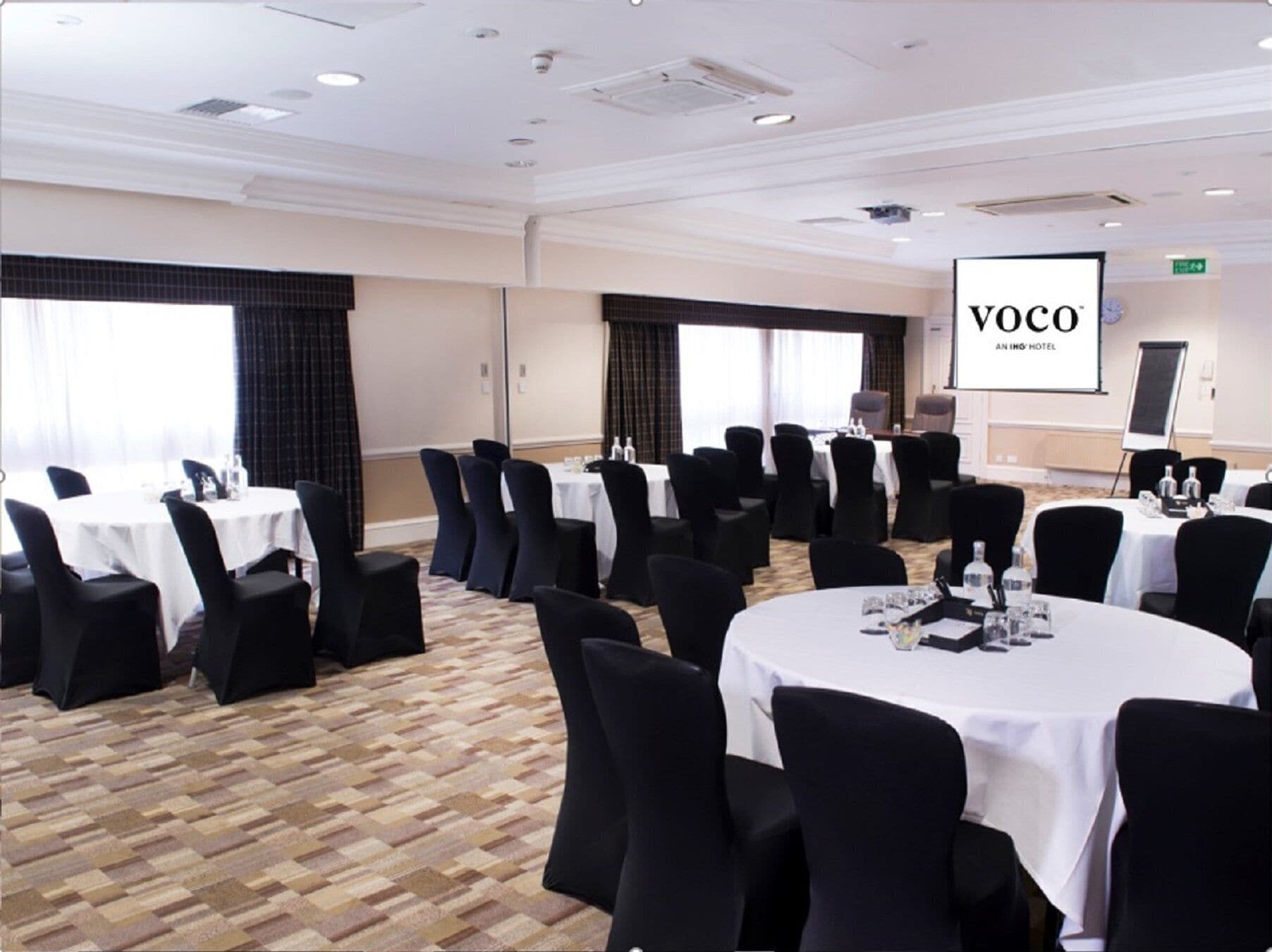A conference room with round tables, black chairs, and white tablecloths.