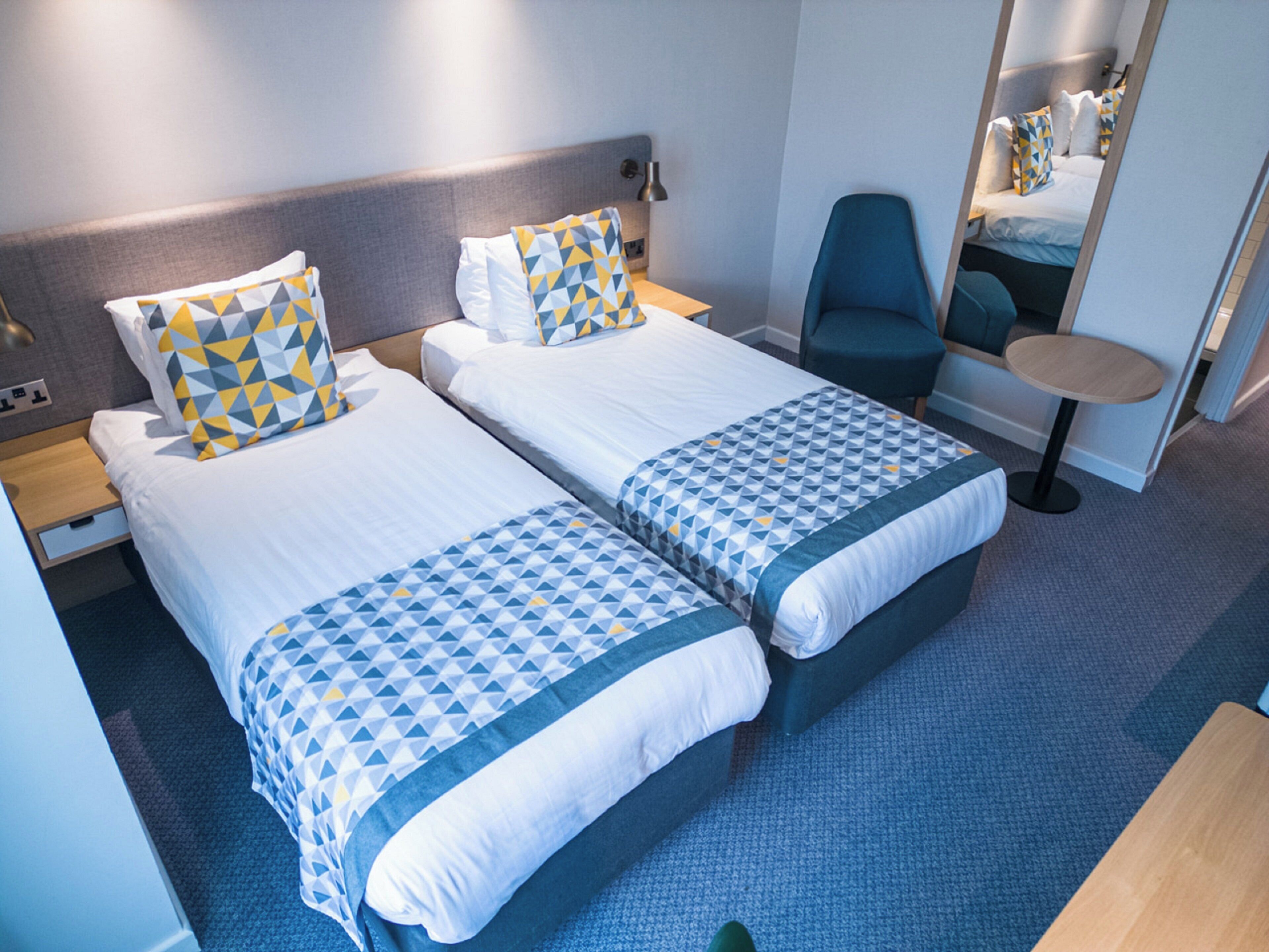 Habitación de hotel con dos camas, una silla, una mesita y un espejo.