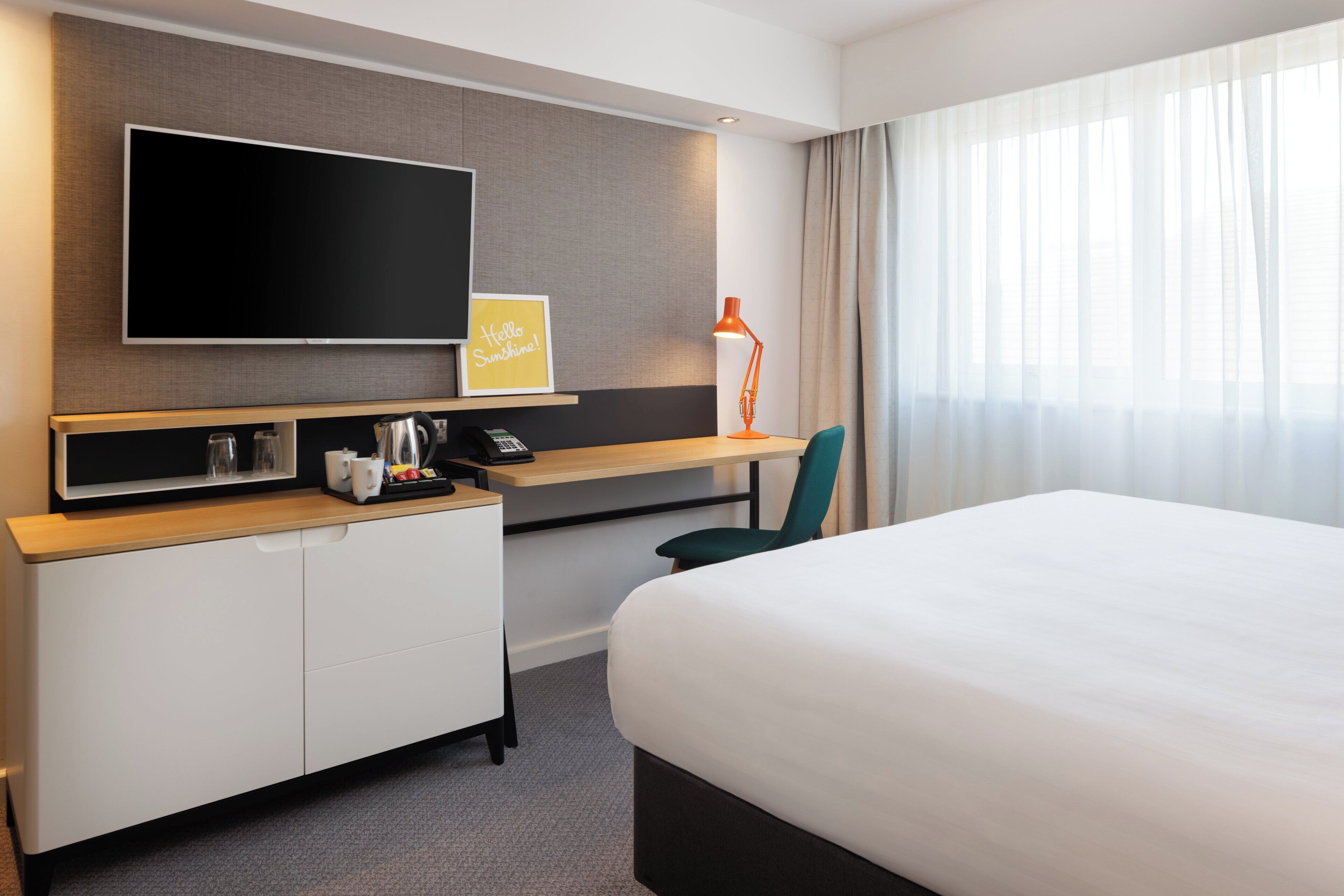Een hotelkamer met een groot bed, een bureau met een flatscreen-tv, een koffiezetapparaat en een stoel.