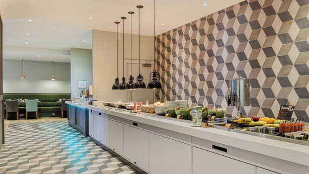 A modern kitchen area with a breakfast bar, geometric patterned wall, and various food items displayed. - Holiday Inn Mansfield - Alfreton by IHG (Alfreton)