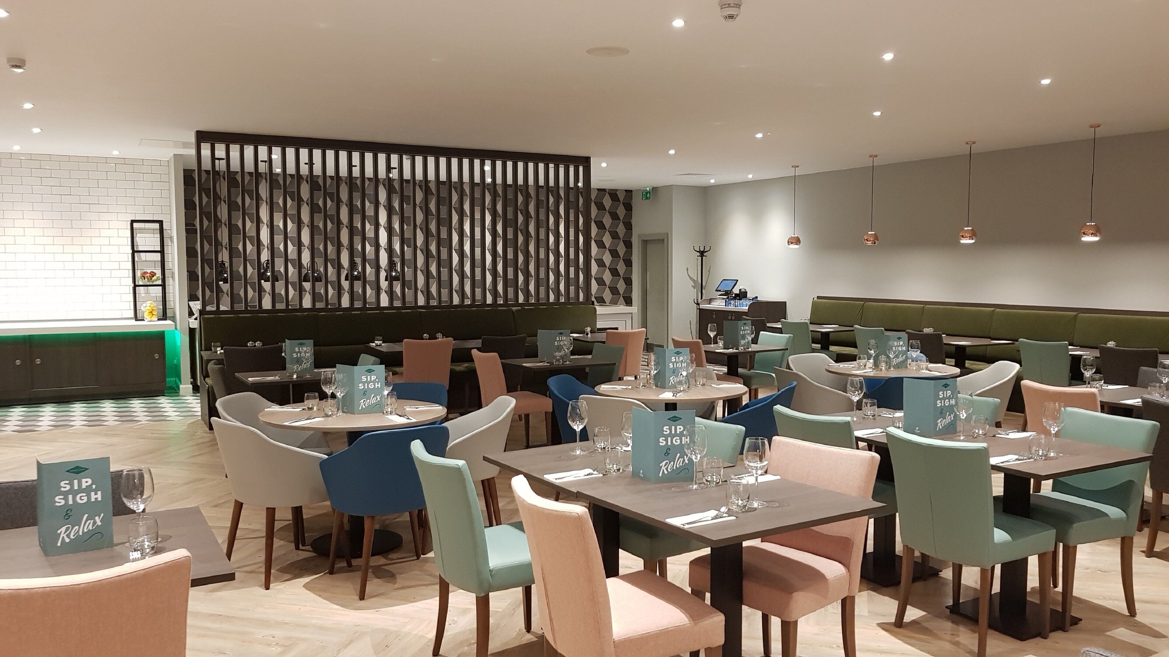 Ein modernes Restaurant mit mehreren Tischen, Stühlen, einer Wand mit Muster und einer grünen Sitzecke.